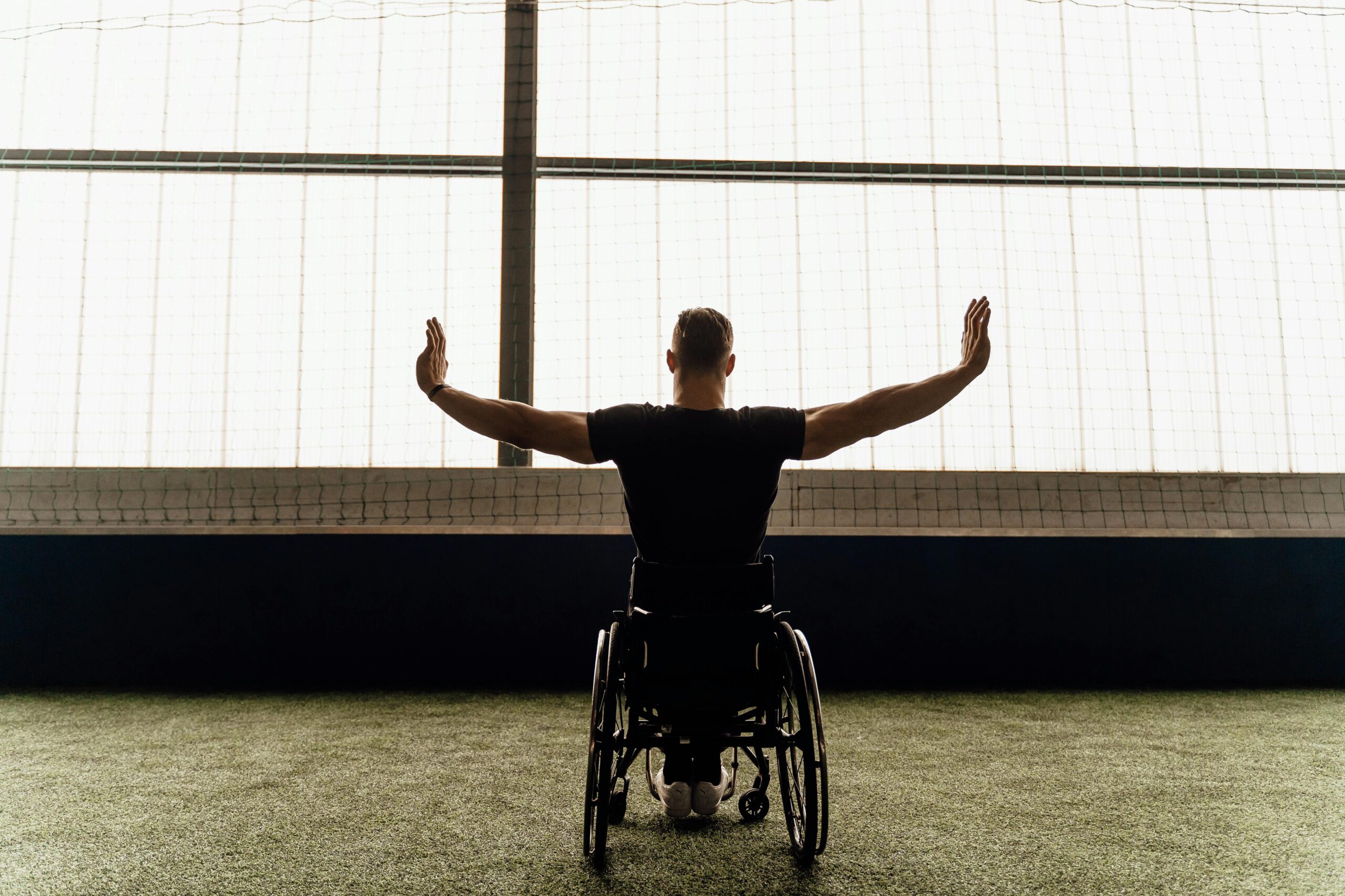 A man in a wheelchair with arms raised indoors, conveying empowerment and inspiration.